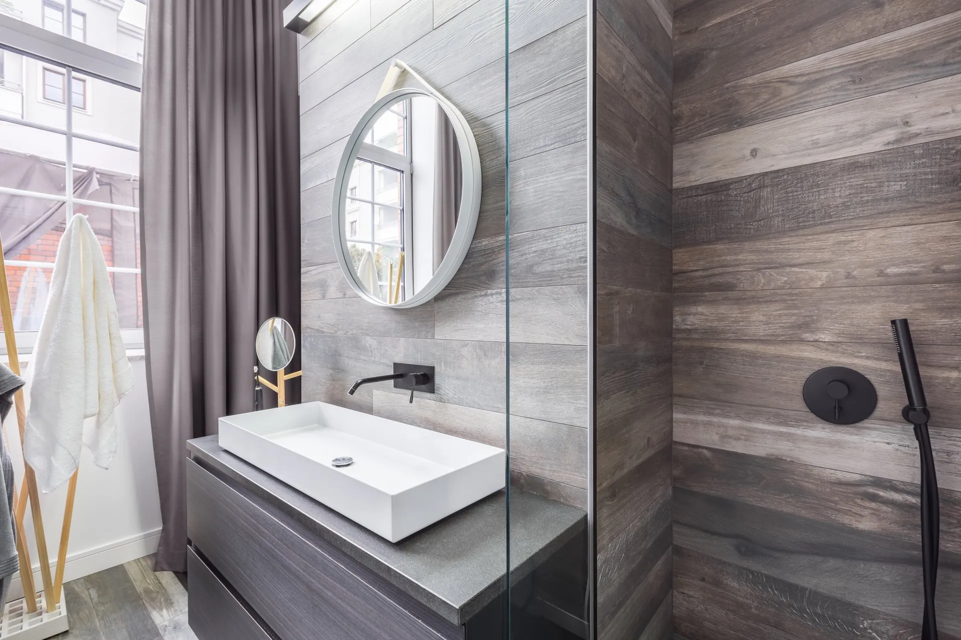 Modern bathroom with wood-like tile, round mirror, and glass shower enclosure