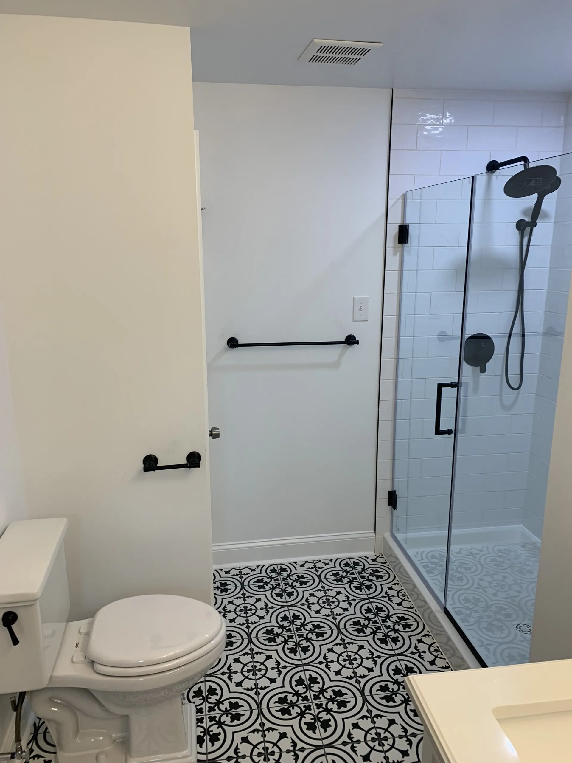 A modern bathroom with white walls, black hardware, and a patterned tile floor