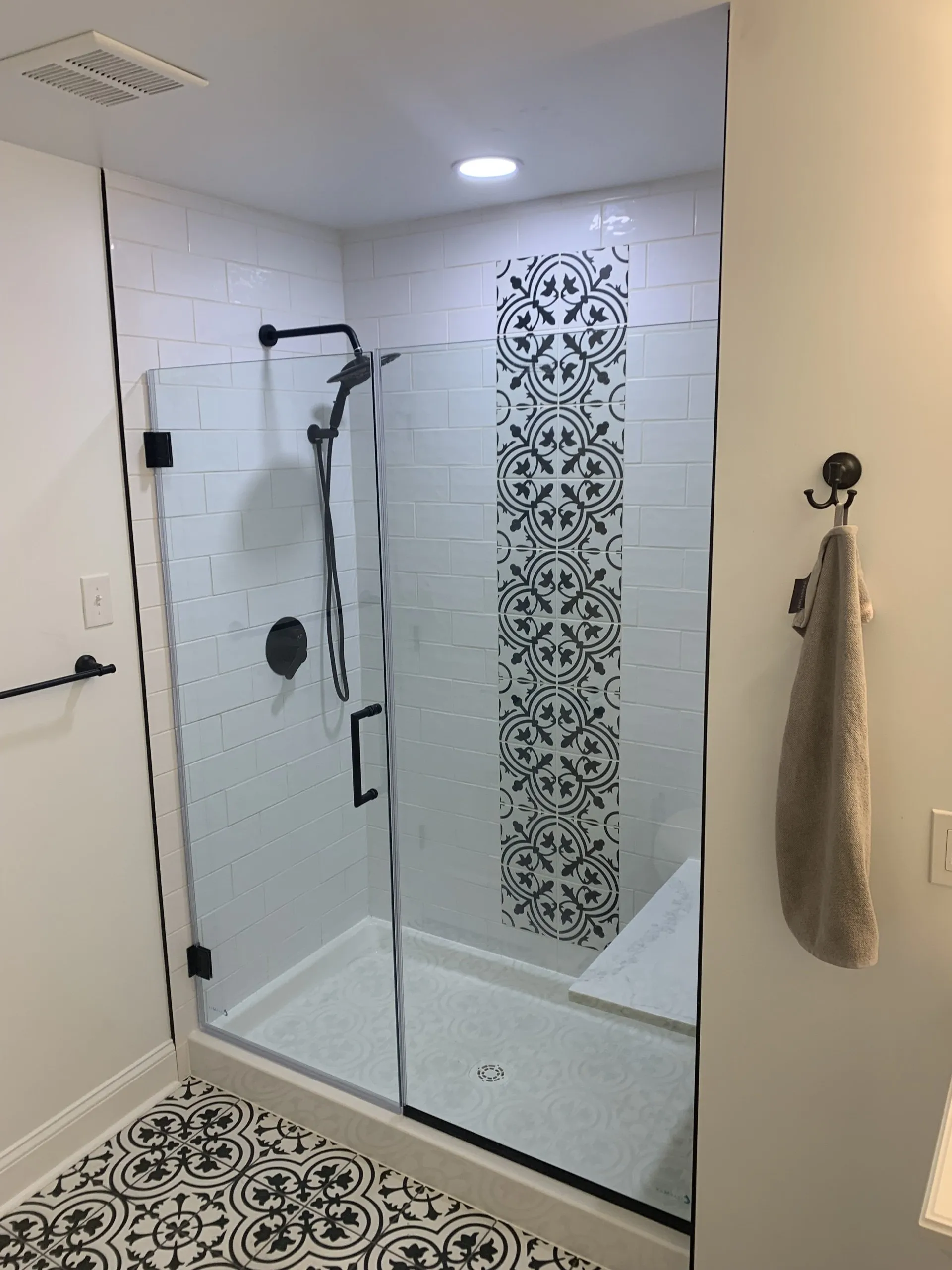 A modern bathroom with a glass shower enclosure, black hardware, and a patterned tile accent wall